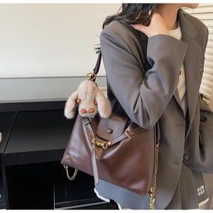 Detail of dark brown tote bag with matte leather texture, gold chain and plush bunny charm