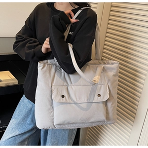 Detail of light grey quilted tote bag featuring front pocket with bronze metal snap buttons