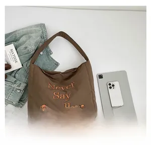 Deep brown nylon tote bag with Never Say Goodbye embroidery on a casual denim background