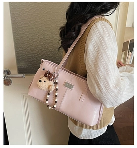 Detail of pink leather tote bag featuring a cute teddy bear charm and metal logo plaque