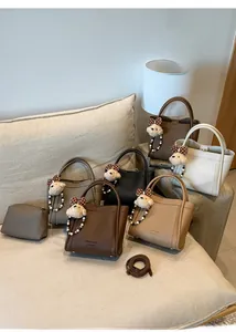 Close-up of textured leather handbags in neutral colors with plush bear charm detail