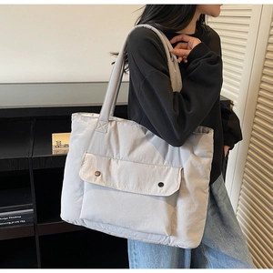 Detail of light blue quilted tote bag showing the front flap pocket and black snap buttons