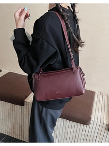 Detail of the dark burgundy leather shoulder bag with a gold embossed logo and strap