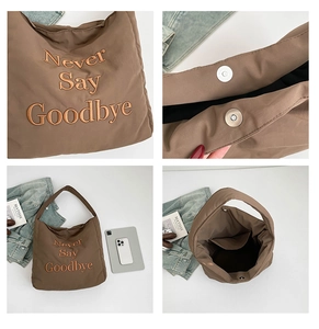 Detail view of brown tote bag featuring 'Never Say Goodbye' embroidery and magnetic closure