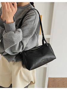 Detail shot of black pebbled leather baguette bag with gold zipper and minimalist logo