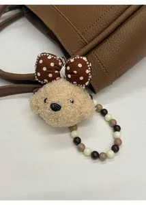 Detail of plush bear bag charm with polka dot bow and beaded strap on a leather bucket bag