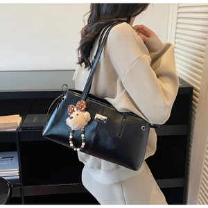 Detail of minimalist black PU leather shoulder bag with cute teddy bear charm accessory