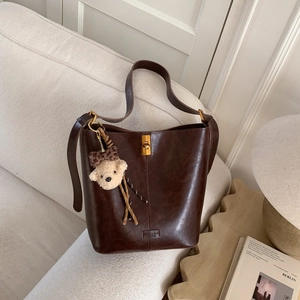 Detailed shot of dark brown leather bucket bag with gold hardware and plush bear charm