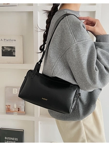 Detailed view of a sleek black leather underarm bag with gold logo on a model
