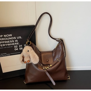 Detail of dark brown leather tote featuring gold lock and plush rabbit pendant charm