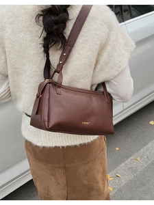 Detail of a deep brown leather underarm bag with gold rivets on a wide shoulder strap