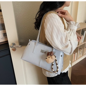 Detail of light blue leather tote bag featuring a plush bear charm and beaded chain