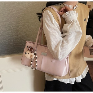 Detail of pink faux leather tote bag with plush bear charm and silver metal logo tag