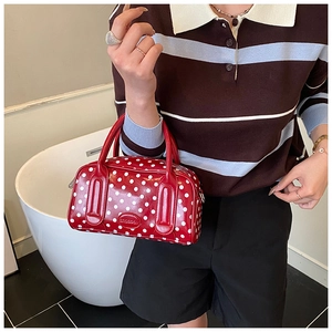 Close-up of a red polka dot Boston handbag featuring dual handles and a retro polished finish