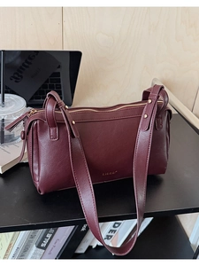 Detail of burgundy baguette bag with matte leather texture and gold hardware logo