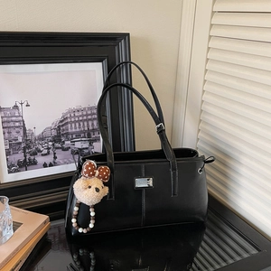 Close-up of black glossy tote bag featuring a silver plaque and a cute teddy bear charm