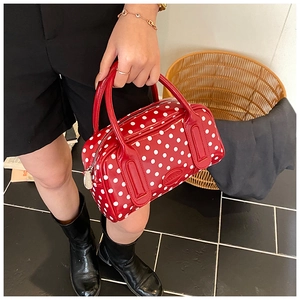Close-up of red polka dot patent leather Boston bag held by model in a street style shot