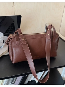 Detail of dark brown leather Boston bag with gold rivets and LULU logo on office desk