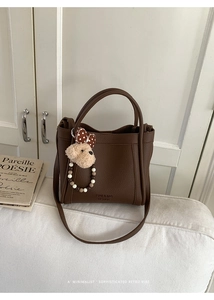 Detail of dark brown lychee grain bucket bag with cute plush bear charm on a sofa
