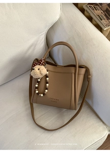 Close-up of brown litchi pattern bucket bag with teddy bear charm on white sofa