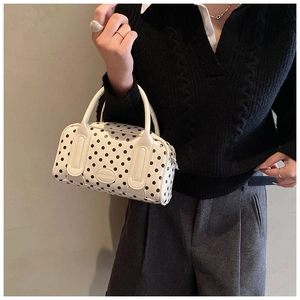 Chic white Boston handbag with black polka dots and dual handles shown on a model