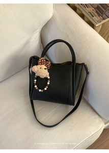 Detail of black pebbled leather bucket bag with cute plush bear charm on white sofa