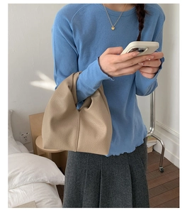 Gros plan d'un sac à main beige en cuir grainé porté par un mannequin en intérieur