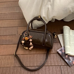 Detail of a shiny dark brown cylindrical handbag with beaded charm on wooden floor