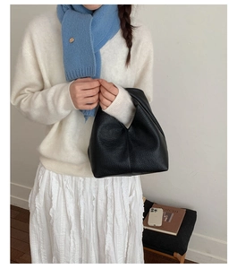 Détail d'un sac seau en cuir noir grainé assorti à une tenue blanche élégante et moderne