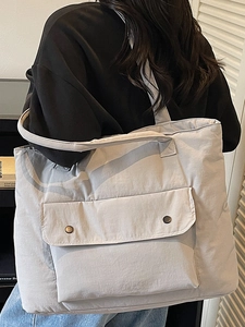 Minimalist light gray tote bag with large front pocket shown on shoulder in interior setting