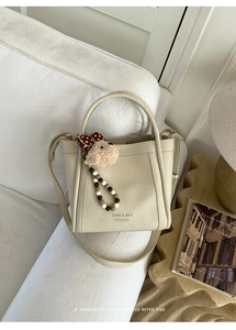 Detail of off-white lychee leather bucket bag with bear charm and beaded chain on a sofa