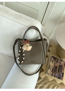 Detail of brown leather bucket bag with plush bear charm and beaded chain on sofa