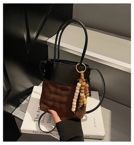 Detail of a chic bucket bag with black leather, brown suede, and decorative wooden beads