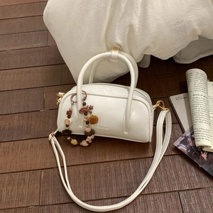 Detail view of cream-colored minimalist handbag with beaded charm and gold hardware
