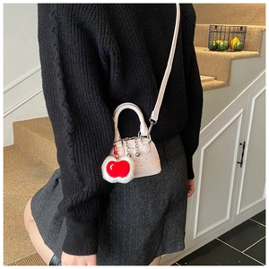 Detail view of mini pink crossbody bag with cherry charm shown on a female model outfit