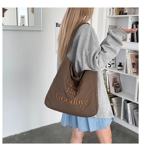 Detailed close-up of brown tote bag with Never Say Goodbye orange 3D embroidery