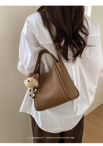 Close-up of brown litchi pattern leather bucket bag with cute plush teddy bear charm