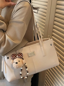 Minimalist beige oversized tote bag in synthetic leather with a cute bear charm and metal tag