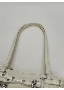 Détail du sac crème brillant avec anses fines et boucles métalliques argentées