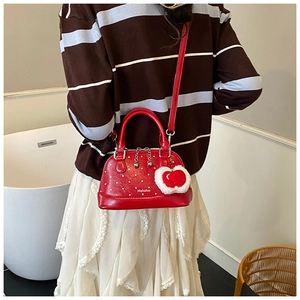 Detail of red polka dot shell bag with glossy finish and heart plush charm on strap