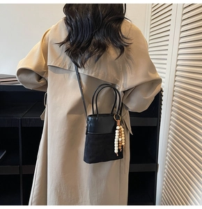 Detail of a black bucket bag with quilted texture and natural wooden bead tassel accent