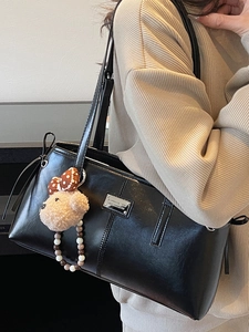 Minimalist black tote bag with plush bear charm and metallic brand plaque on shoulder strap