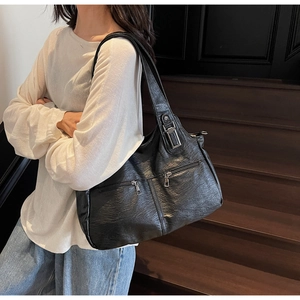 Detail of black textured leather tote bag with functional zippers on wooden stairs