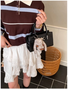 Détail d'un sac bandoulière en cuir noir avec serrure argentée et pendentif lapin en peluche