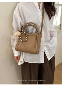 Close-up of khaki bucket bag with litchi texture, plush ball and bead charms