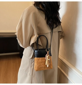 Detail view of mini two-tone quilted bucket bag with wooden bead tassel on a model