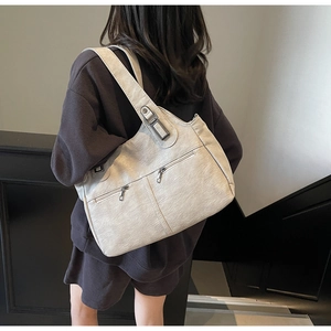 Detail view of a cream vintage textured tote bag with double zippers on back of a model