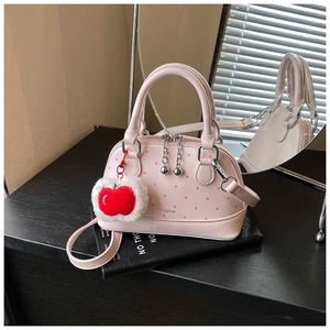 Detail of pink polka dot shell bag featuring a plush red apple charm and metal zip puller