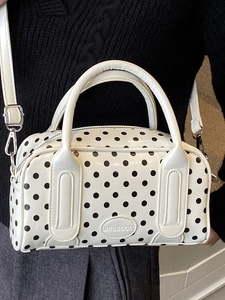 White polka dot handbag with black spots and detachable strap shown on a model