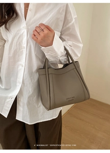 Detail of taupe lychee texture bucket bag with embossed logo held by model